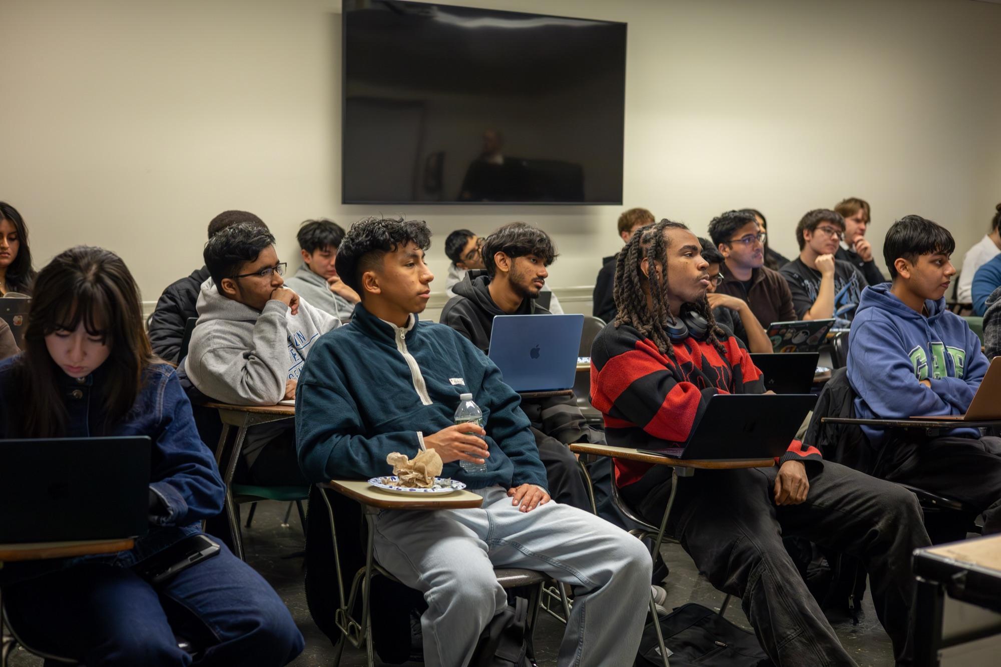 Students sitting with open laptops, listening during a Cybersecurity Reach Foundation session